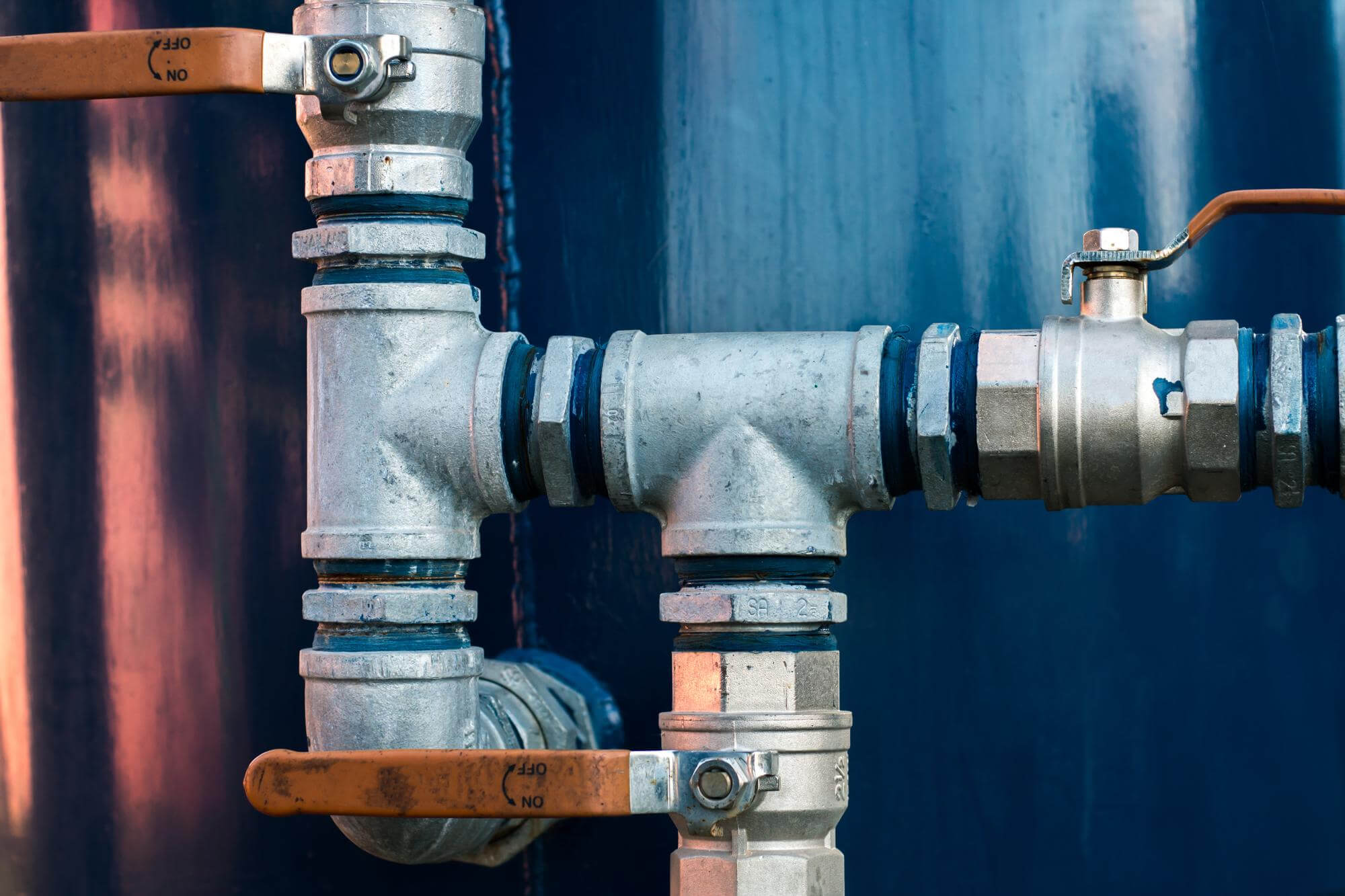 Metalliset putket ja venttiilit sinisellä taustalla, valaistus on kirkas ja yksityiskohdat näkyvät selvästi.